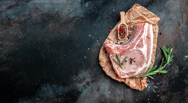 Bio-Schweinefleisch-Chop-Set mit Gewürzen und Rosmarin und rotem Pfeffer auf schwarzem Tisch Lange Banner-Format-Draufsicht