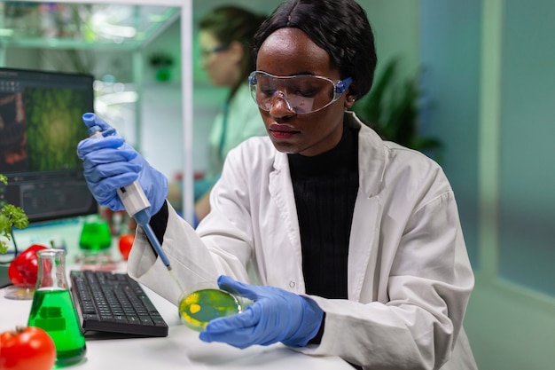 Biólogo científico investigador mujer africana tomando solución genética del tubo de ensayo