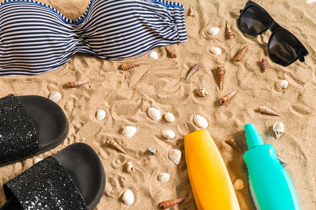 Biquíni de verão e acessórios elegantes conjunto de praia, biquíni de praia e areia do mar como fundo, vista de cima, conceito