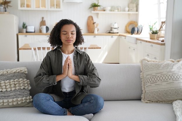 Biracial Frau praktiziert Yoga zu Hause sitzend in Lotus-Pose auf dem Sofa Meditation gesunder Lebensstil