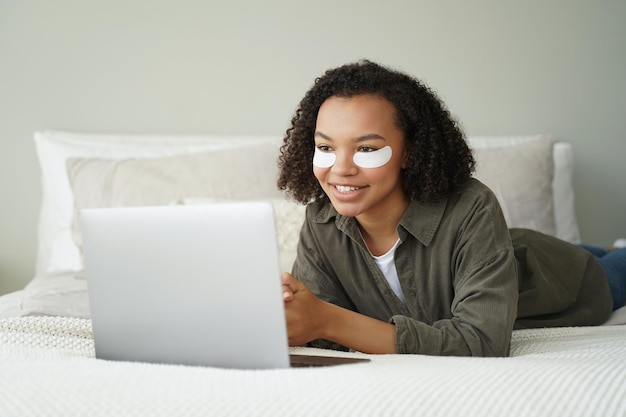 Biracial Mädchen mit Augenflecken auf dem Gesicht arbeiten am Laptop Schönheit der morgendlichen Gesichtspflegeroutine