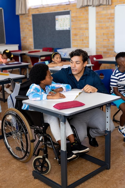 Biracial männlicher Lehrer mit Junge im Rollstuhl in der Klasse an der Grundschule