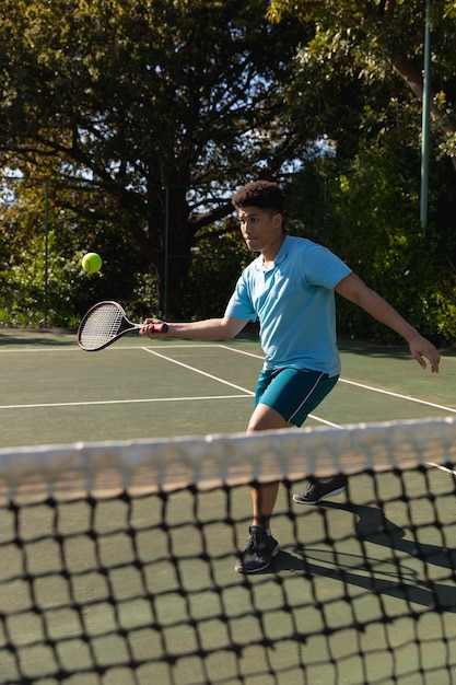 Biracial Mann spielt Tennis und wirft den Ball über das Netz auf einem sonnigen Tennisplatz im Freien zurück. Inklusivität, Sport, gesunde Hobbys, Wettbewerb, Fitness und Freizeitkonzept.