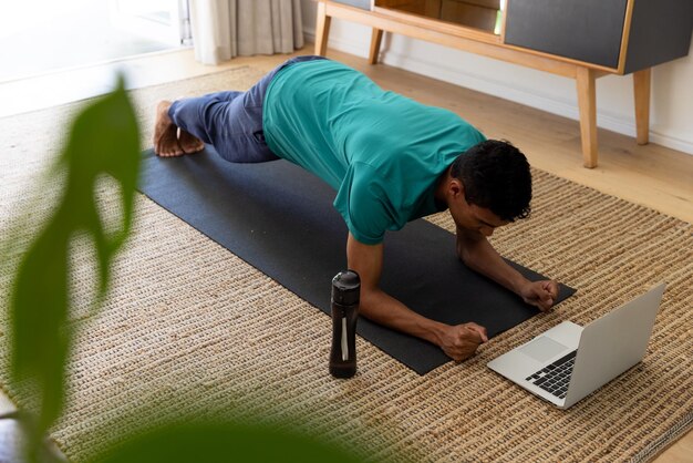 Biracial Mann trainiert auf Matte und benutzt Laptop zu Hause