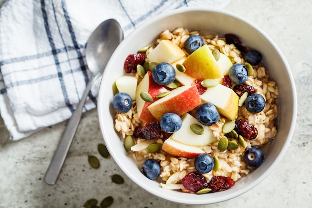 Bircher muesli o avena durante la noche con manzana, plátano y arándanos en un tazón gris, vista desde arriba.