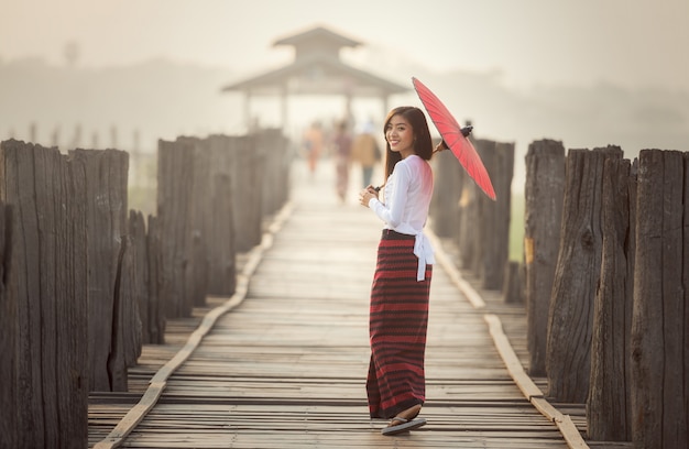 Birmanische Frau, die traditionellen roten Regenschirm hält und auf Brücke U Bein, Myanmar geht