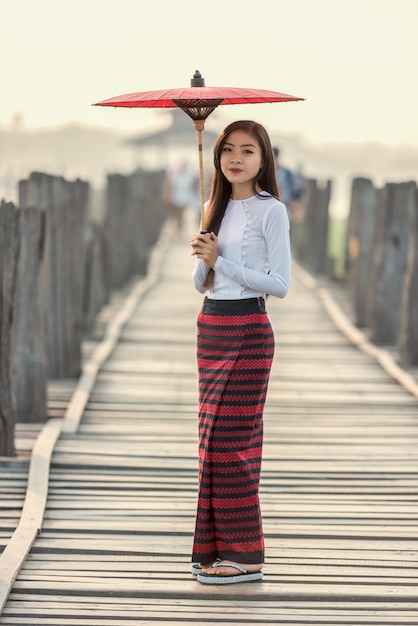 Birmanische Frau, die traditionellen roten Regenschirm hält und auf Brücke U Bein, Myanmar geht