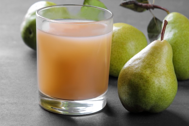 Birnensaft in einem Glas und frische reife Birnen auf einem schwarzen Tisch. Nahaufnahme