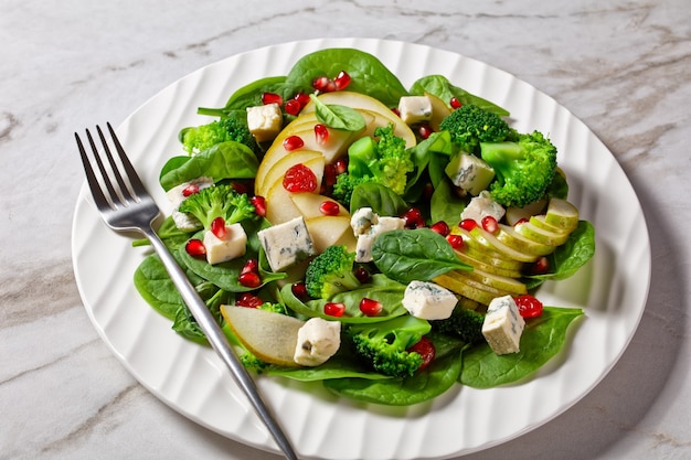 Birnensalat mit Blauschimmelkäsewürfeln, Brokkoli, Spinat, getrockneten Cranberry- und Granatapfelkernen auf einem Teller auf einem Marmortisch, Thanksgiving-Beilage, horizontale Ansicht von oben