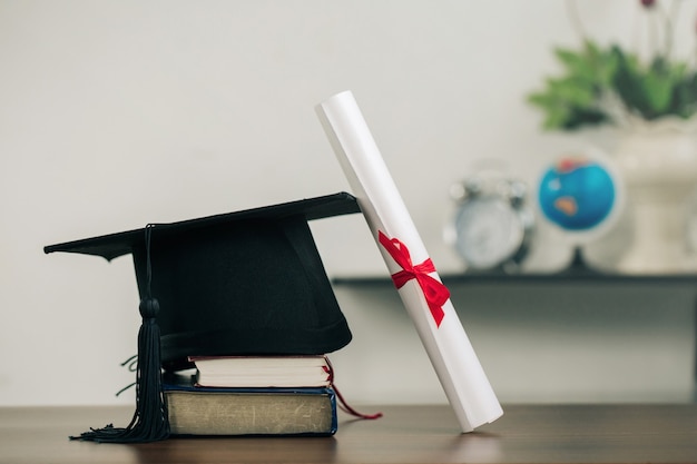 Un birrete en libros y desplazamiento de graduación en el escritorio concepto de aprendizaje educativo.