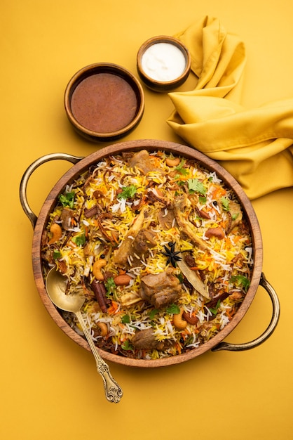 Biryani de cordero indio preparado en arroz basmati servido con salsa de yogur sobre fondo cambiante, enfoque selectivo