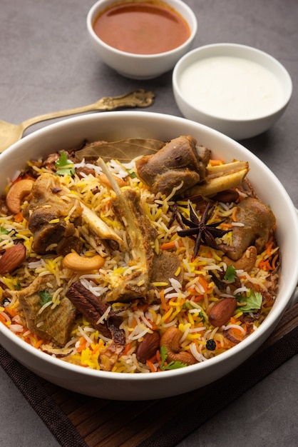 Biryani de cordero indio preparado en arroz basmati servido con salsa de yogur sobre fondo cambiante, enfoque selectivo