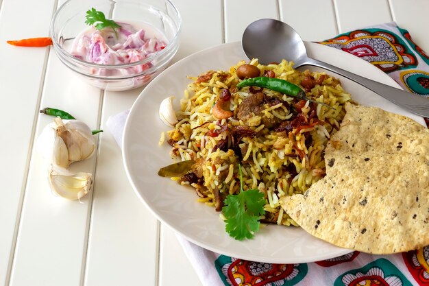 Biryani de carneiro indiano tradicional servido com raita e pappadam crocante em superfície branca Foco seletivo Cozinha autêntica