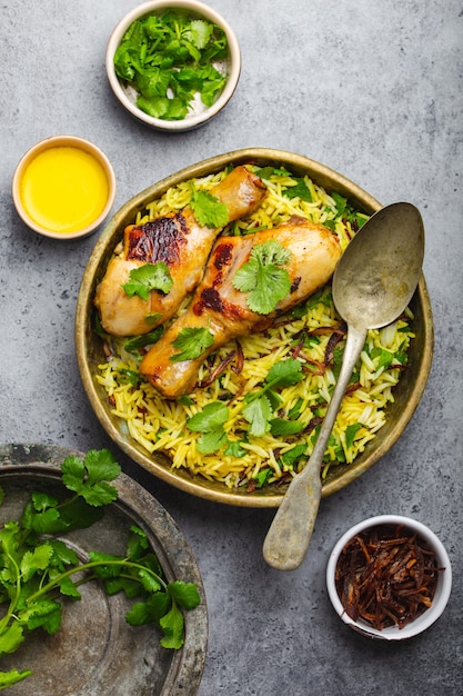 Biryani-Huhn, traditionelles Gericht der indischen Küche, mit Basmatireis, gebratenen Zwiebeln, frischem Koriander in Schüssel auf grauem rustikalem Steinhintergrund. Authentisches indisches Essen, Draufsicht, Nahaufnahme