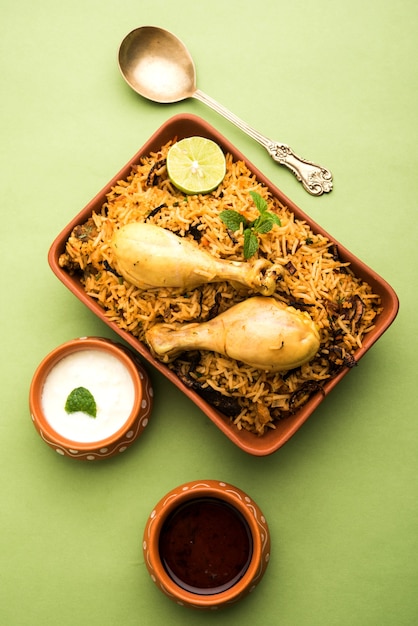 Biryani de pollo indio servido en un cuenco de terracota con yogur sobre fondo blanco. enfoque selectivo