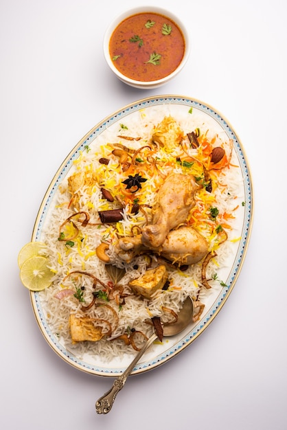 Biryani de pollo indio servido en un cuenco de terracota con yogur sobre fondo blanco. enfoque selectivo