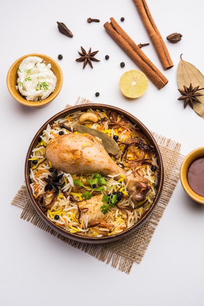 Biryani de pollo picante estilo restaurante en tazón de madera con Raita y salan, comida popular de la India o Pakistán