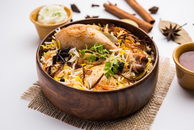 Biryani de pollo picante estilo restaurante en tazón de madera con Raita y salan, comida popular de la India o Pakistán