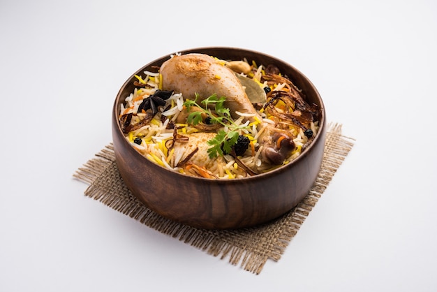 Biryani de pollo picante estilo restaurante en tazón de madera con Raita y salan, comida popular de la India o Pakistán