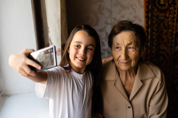 Foto la bisabuela se sienta con su bisnieta y mira el teléfono inteligente. la abuela y el niño se toman un selfie en un teléfono inteligente. la abuela con su nieta miran el teléfono.