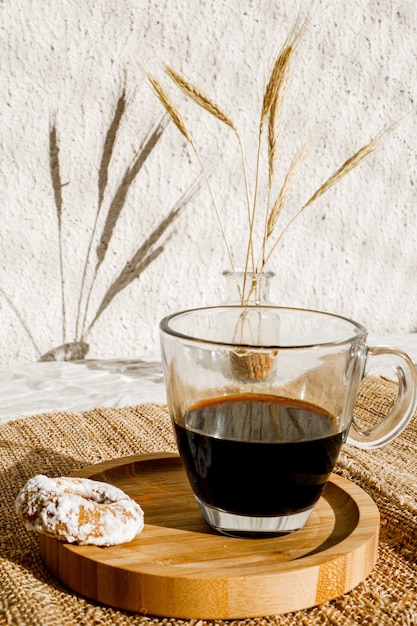 Biscoito amanteigado com açúcar de confeiteiro por cima e uma xícara de café preto. Luz forte com sombras nítidas. Foco seletivo.