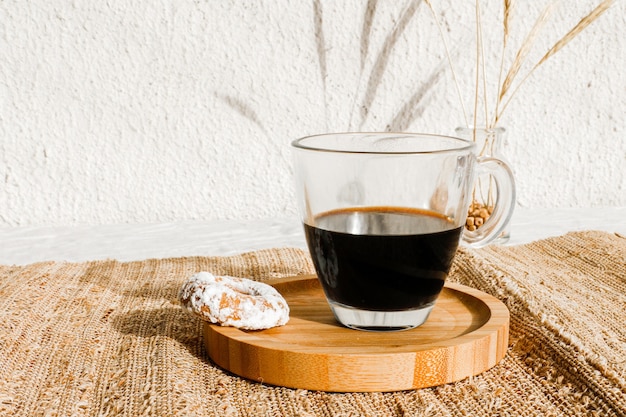 Biscoito amanteigado com açúcar de confeiteiro por cima e uma xícara de café preto. Luz forte com sombras nítidas. Foco seletivo.