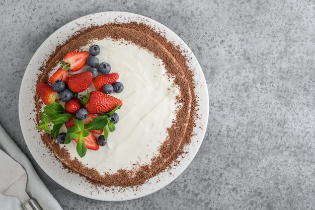 Biscoito de bolo caseiro com mascarpone decorado com chocolate ralado, morango fresco e mirtilos em cinza