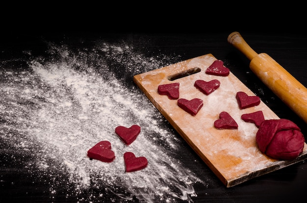 Biscoito de coração vermelho e um pedaço de massa na placa de madeira, assando no dia dos namorados