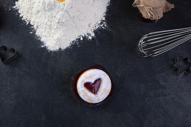 Biscoito de pastelaria com um coração vermelho jam e açúcar em pó de confeiteiro