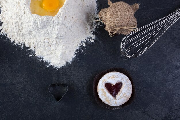 Biscoito de pastelaria com um coração vermelho jam e açúcar em pó de confeiteiro