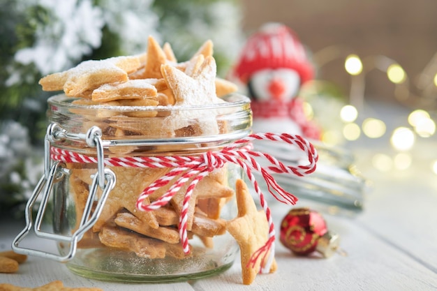 Biscoitos amanteigados de Natal ou estrelas de gengibre com fita vermelha decoração festiva bolas de abeto e guirlanda de luz Biscoitos alemães tradicionais Tradições de celebração de Natal culinária familiar