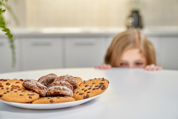 Biscoitos americanos no prato, criança se escondendo atrás da mesa.