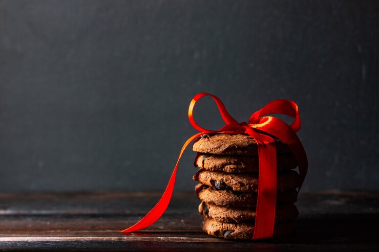 Foto biscoitos caseiros com gotas de chocolate amarrados com uma fita vermelha em estilo rústico.