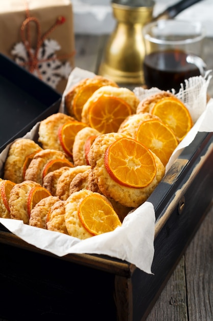 Biscoitos caseiros com tangerinas fatiadas e brinquedos de Natal em uma caixa escura. Foco seletivo.