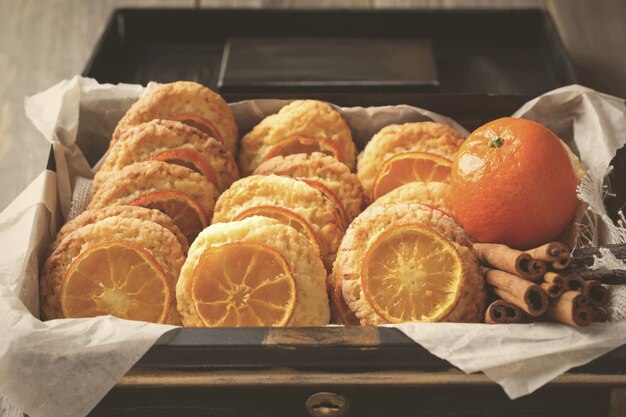 Biscoitos caseiros com tangerinas fatiadas e brinquedos de Natal em uma caixa escura. Imagem tonificada. Foco seletivo.