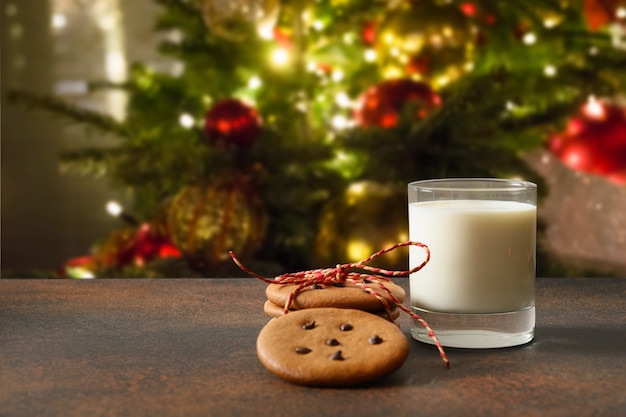 Biscoitos caseiros de Natal e copo de leite para o Papai Noel perto da árvore de Natal