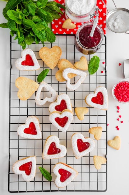 Biscoitos caseiros em forma de coração com geléia de baga e açúcar em pó em uma gradinha com folhas de hortelã