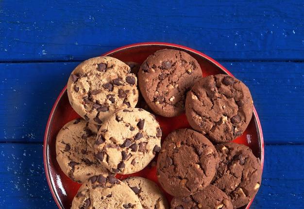 Biscoitos com chocolate e nozes em prato vermelho na mesa de madeira azul vista superior