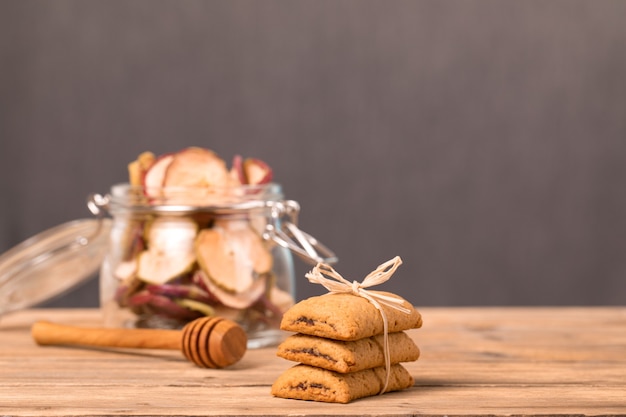 Biscoitos com geléia amarrada com corda, um pote de frutas secas de maçãs e laranjas e uma colher de mel.