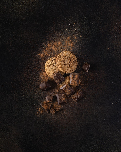 Biscoitos com pedaços de chocolate e chocolate amargo com cacau em uma vista superior de fundo escuro