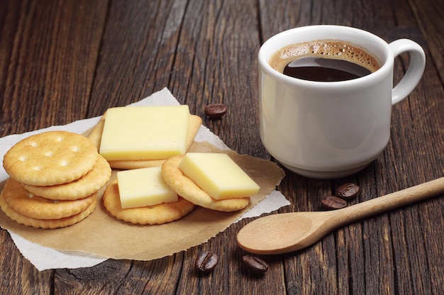 Biscoitos cracker com queijo e xícara de café na velha mesa de madeira