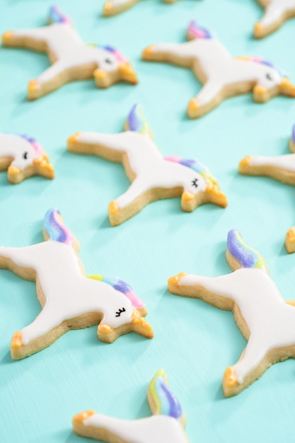 Biscoitos de açúcar de unicórnio decorados com glacê real e glitter de comida em um fundo azul.