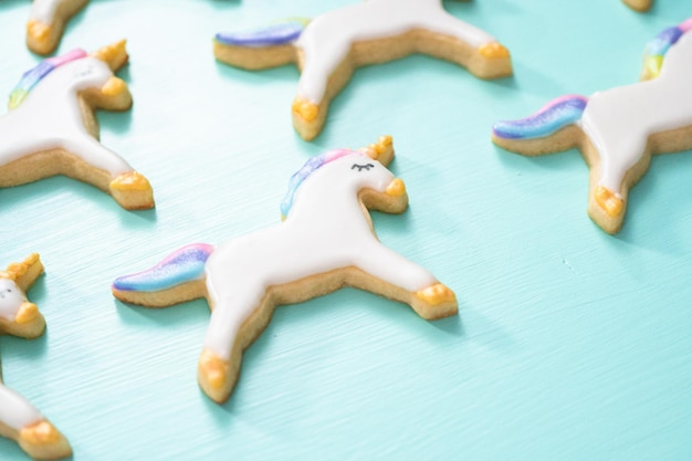 Biscoitos de açúcar de unicórnio decorados com glacê real e glitter de comida em um fundo azul.