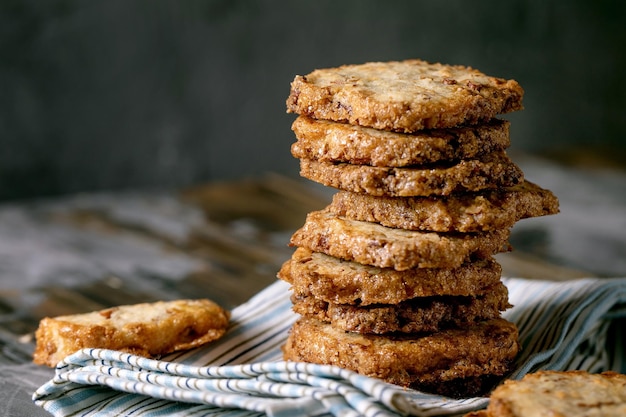 Biscoitos de açúcar shortbread quadrados caseiros com nozes e chocolate branco na pilha na toalha de cozinha de linho na mesa de madeira escura. cozimento doce caseiro. close up, espaço