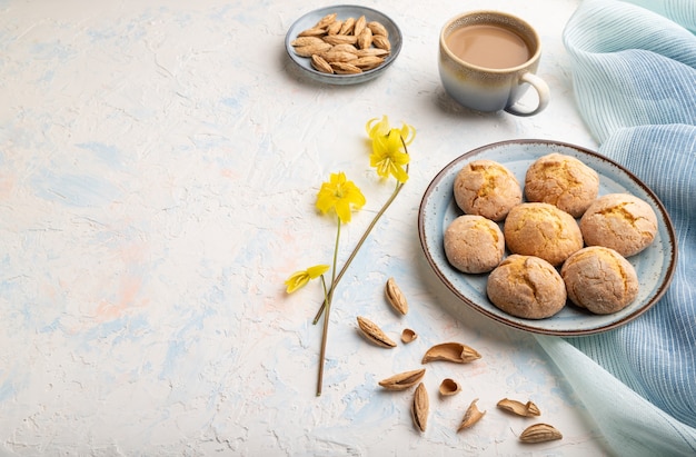 Biscoitos de amêndoa e uma xícara de café em um fundo branco de concreto e têxteis de linho azul.