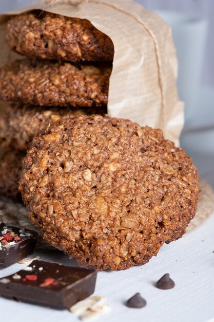 Biscoitos de aveia caseiros com chocolate e nozes amarrados com fio de juta em papel manteiga e fundo branco de madeira