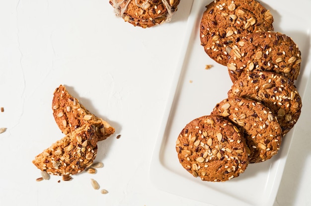 Biscoitos de aveia caseiros com sementes de linho e gergelim em uma mesa branca. Conceito de comida saudável, lanches de café da manhã. Leite e biscoitos. Vida saudável de alimentos ainda. Layout de biscoitos de Natal ou Ano Novo.