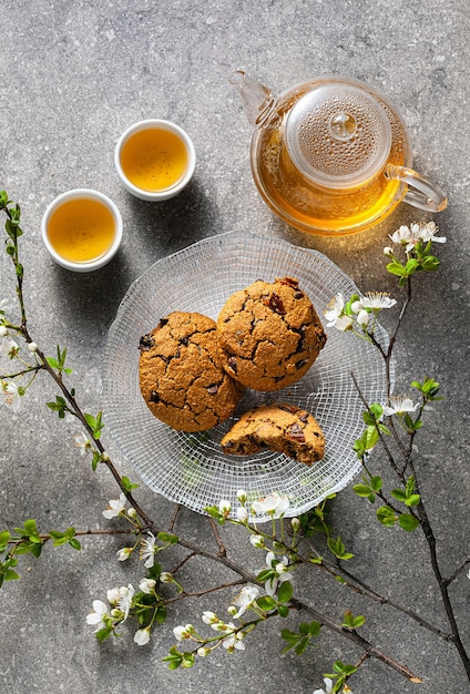 Biscoitos de aveia caseiros em uma mesa com galhos de uma árvore florescendo e chá verde em um bule de vidro.