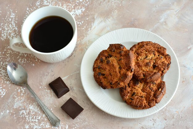 biscoitos de aveia com lascas de chocolate no prato branco com colher de chá e xícara de café, close-up