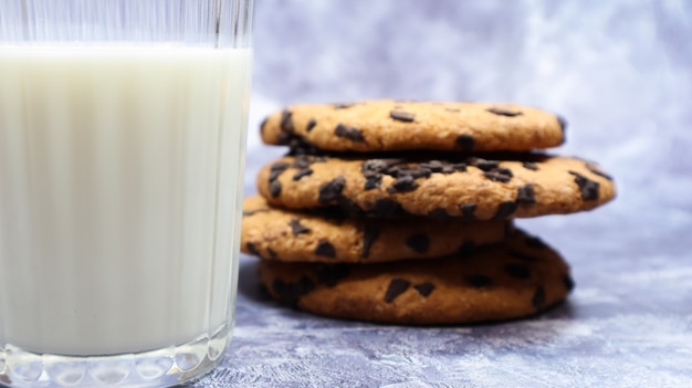 Biscoitos de chocolate americano empilhados uns sobre os outros com leite em um copo em um fundo cinza. massa crocante arredondada tradicional com gotas de chocolate. padaria. sobremesa deliciosa, pastéis.